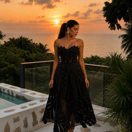 Woman wearing the Midnight Leaf Dress, a black handcrafted strapless midi dress featuring leaf-inspired appliqué details and a sheer flowing skirt.