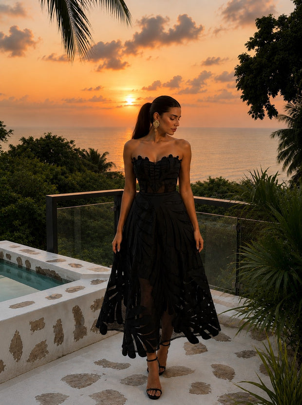 Woman wearing the Midnight Leaf Dress, a black handcrafted strapless midi dress featuring leaf-inspired appliqué details and a sheer flowing skirt.