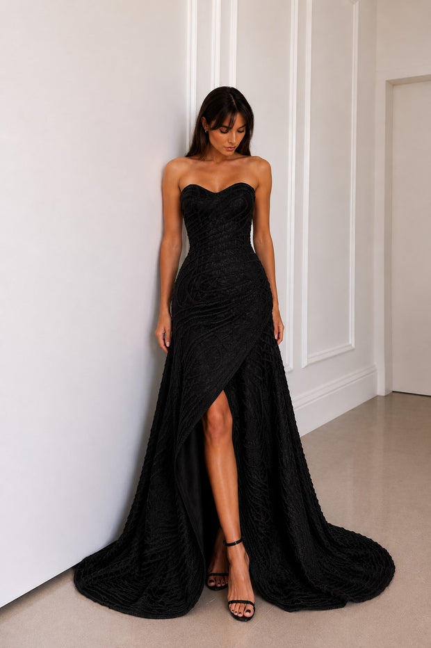 Woman wearing a luxury black strapless evening gown with rope embroidery and a dramatic floor-length train.