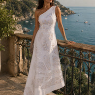 Woman wearing a white one shoulder gown with handcrafted shell embellishments overlooking the sea.