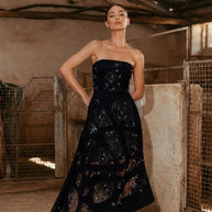 Woman wearing a black one shoulder gown with handcrafted shell embellishments overlooking the sea.