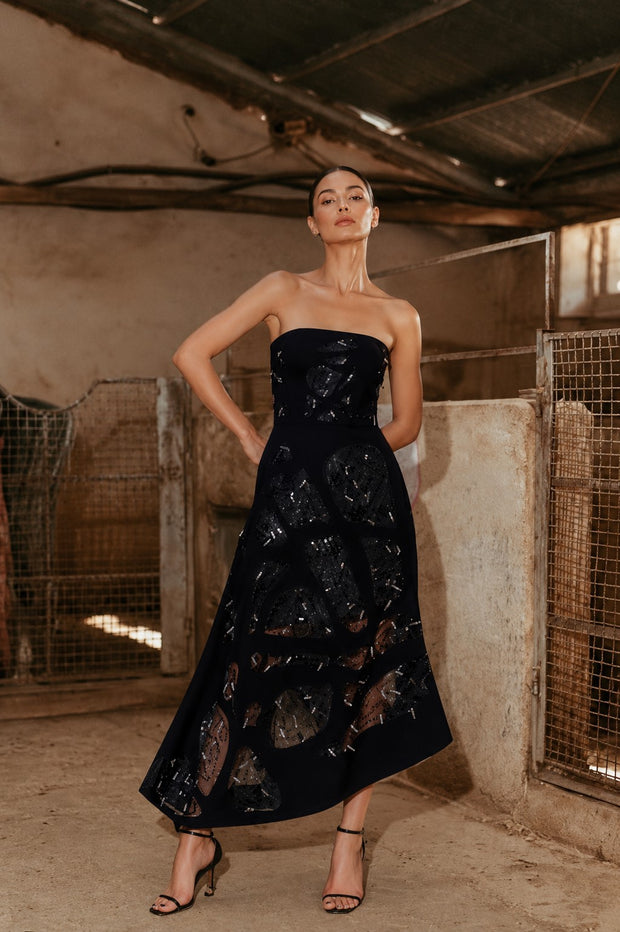 Woman wearing a black one shoulder gown with handcrafted shell embellishments overlooking the sea.